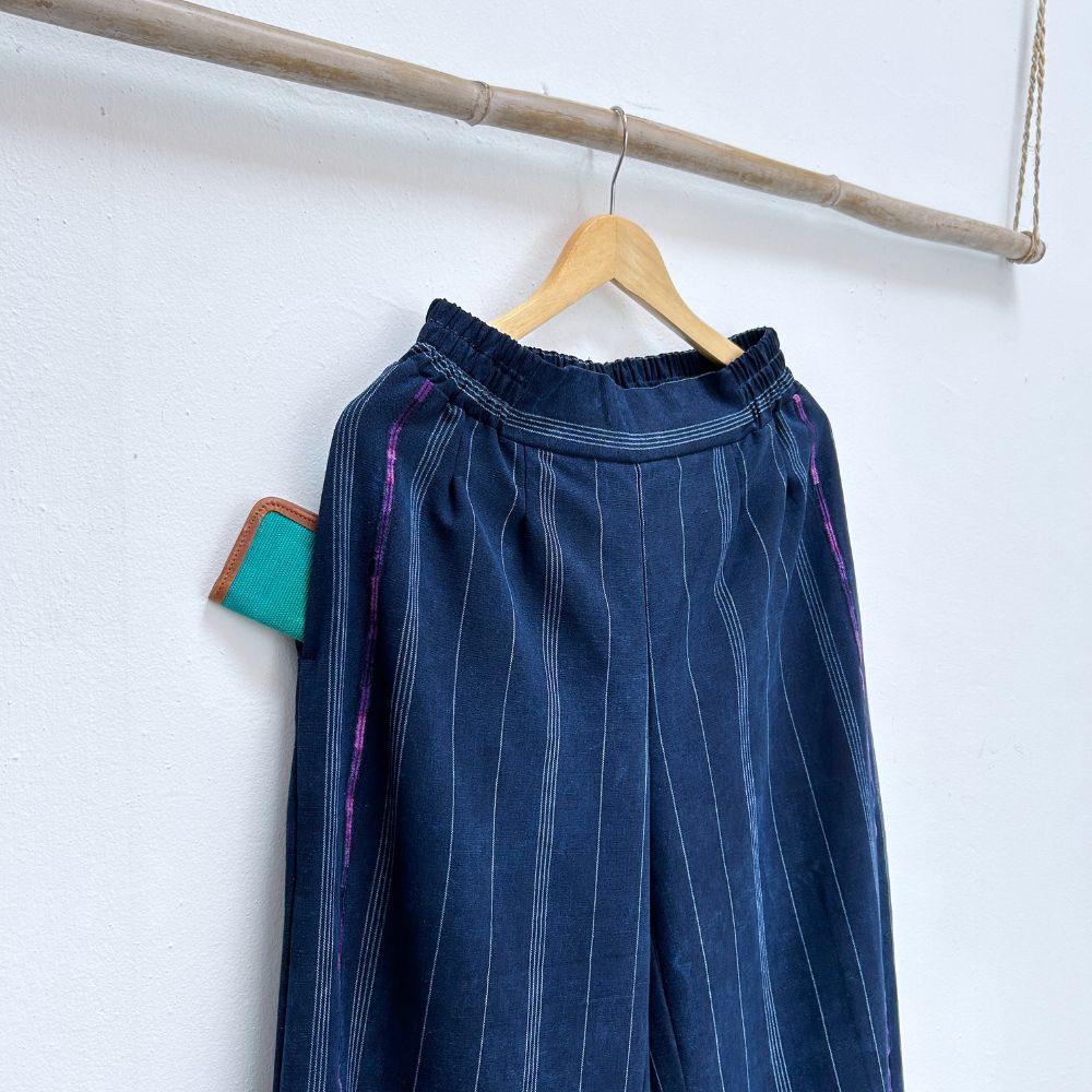 Blue pinstripe corte trousers hanging on a wooden hanger against a white wall.