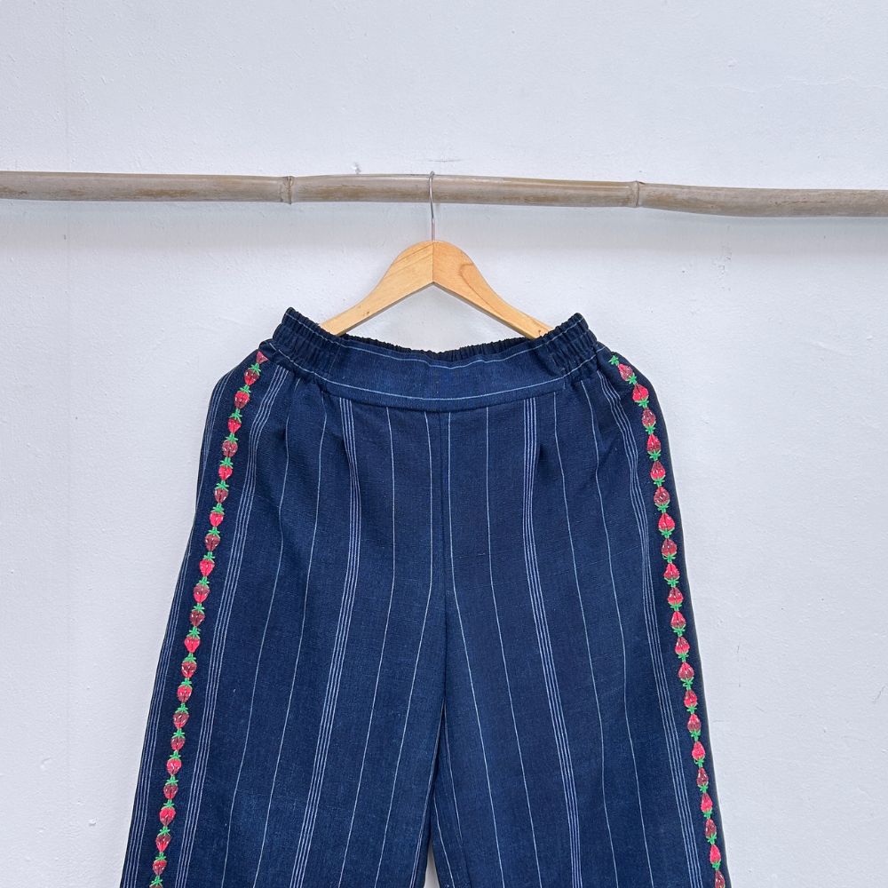 Navy blue pinstripe trousers with strawberries randa embroidery  on a hanger against a white background