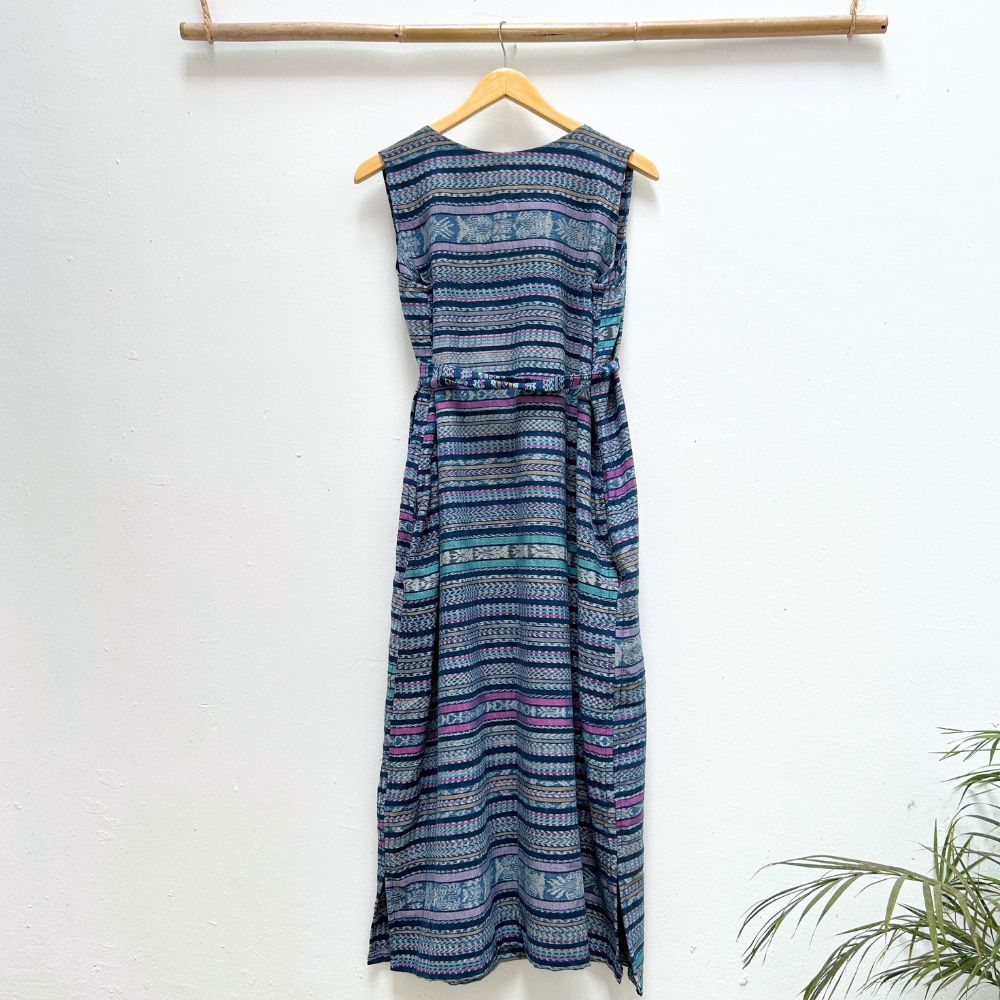 Blue patterned dress hanging on a wooden hanger against a white wall with a plant in the corner.