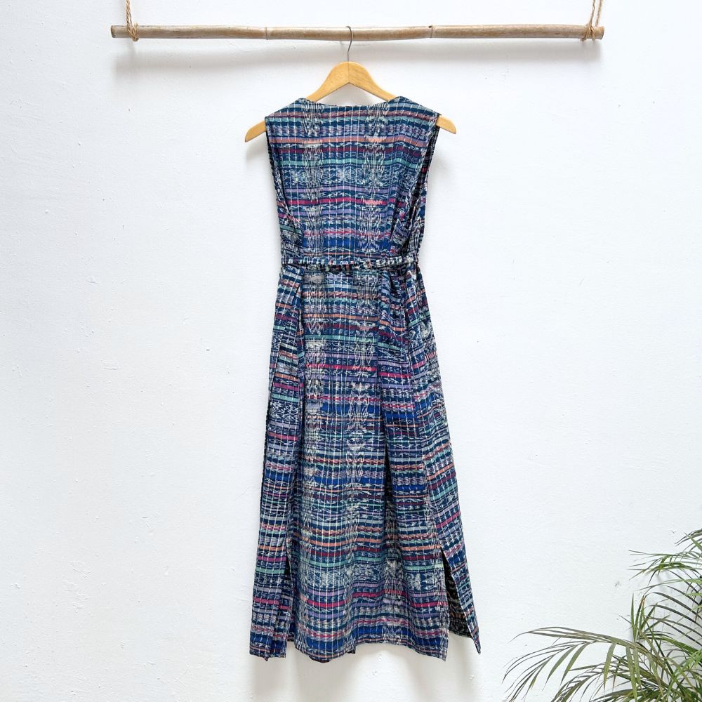Blue patterned dress hanging on a wooden hanger against a white wall with a plant in the corner.