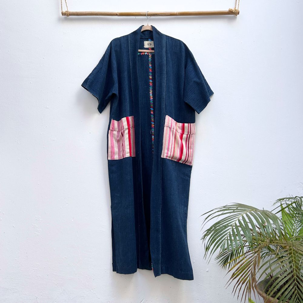 Navy blue duster-style jacket with pink and white patterned pockets on a white wall.