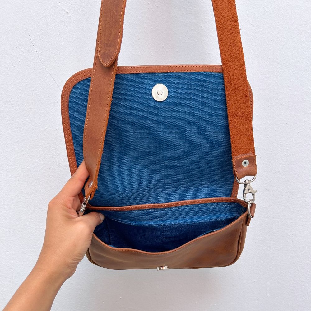 Brown leather crossbody bag with blue interior on a white background