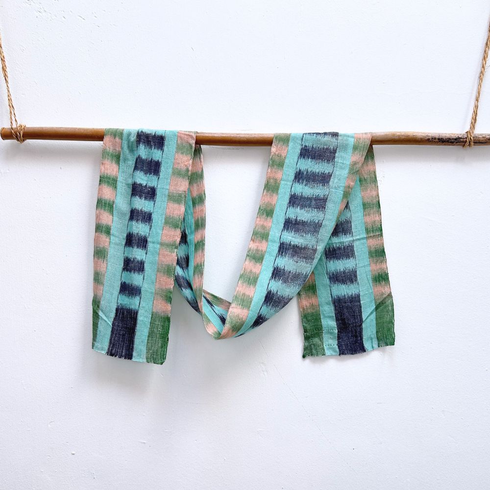 Handwoven natural hues green, pink, and blue hanging on a stick against a white background