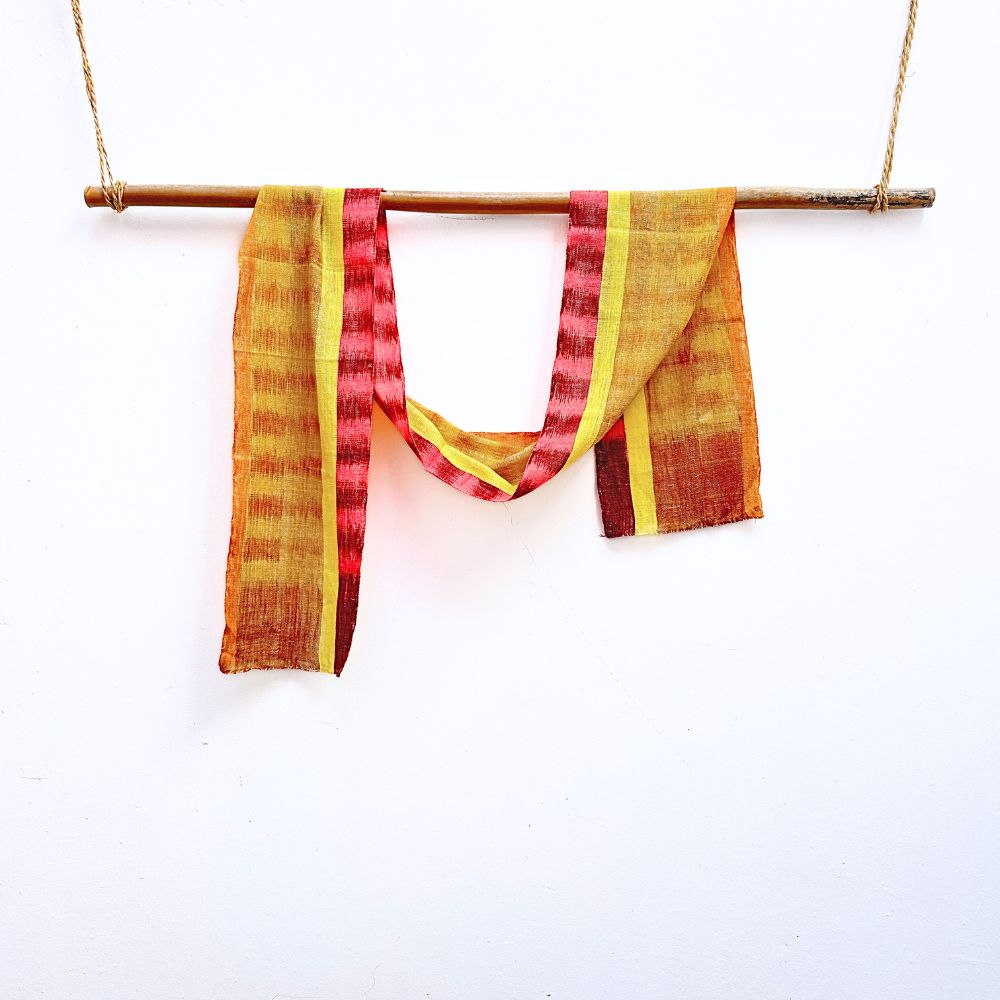 Red and yellow patterned fabric hanging on a stick against a white background