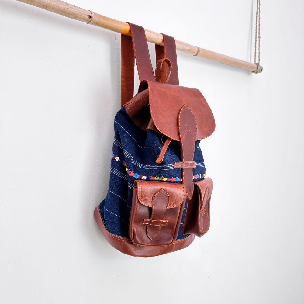 Corte backpack with brown leather straps and pockets hanging on a wooden rod against a white background