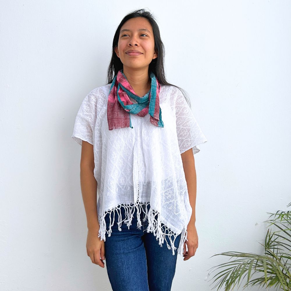 Woman wearing a white top and blue jeans with a colorful scarf around her neck against a white background.