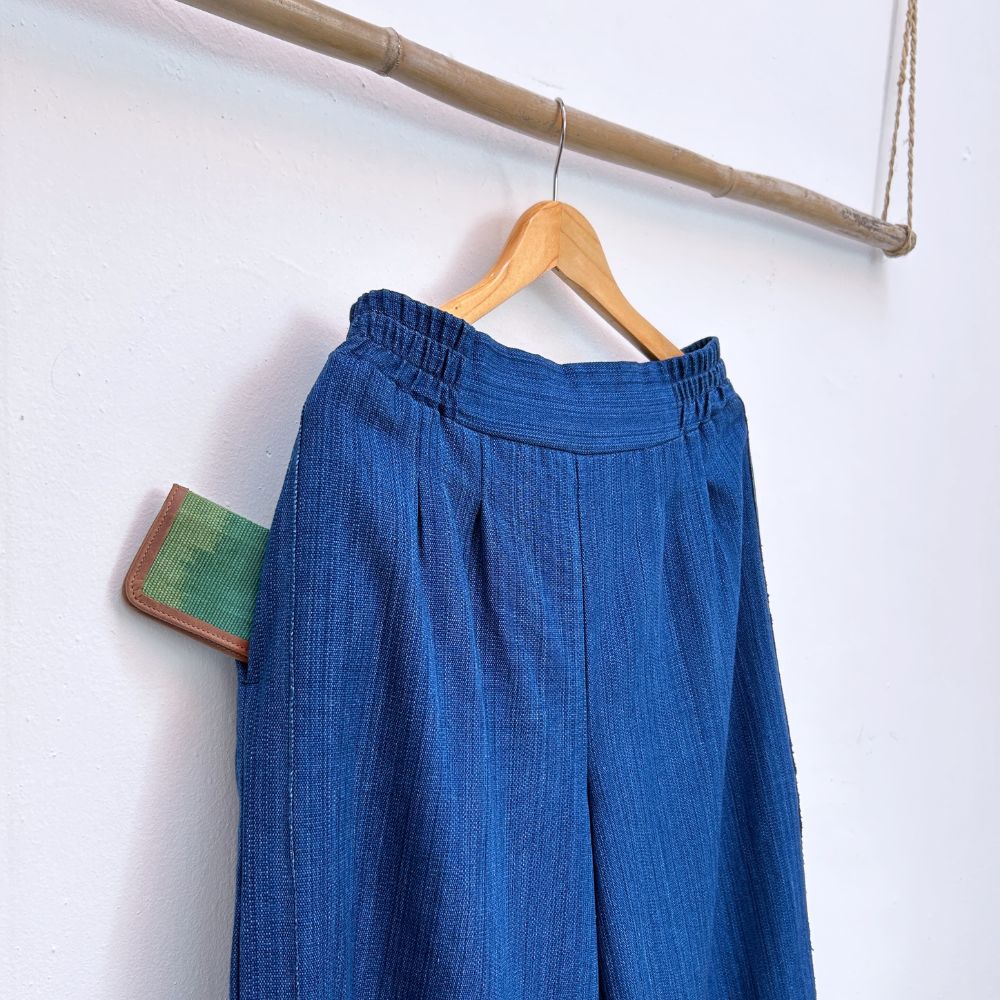 Blue pants hanging on a wooden hanger against a white wall.