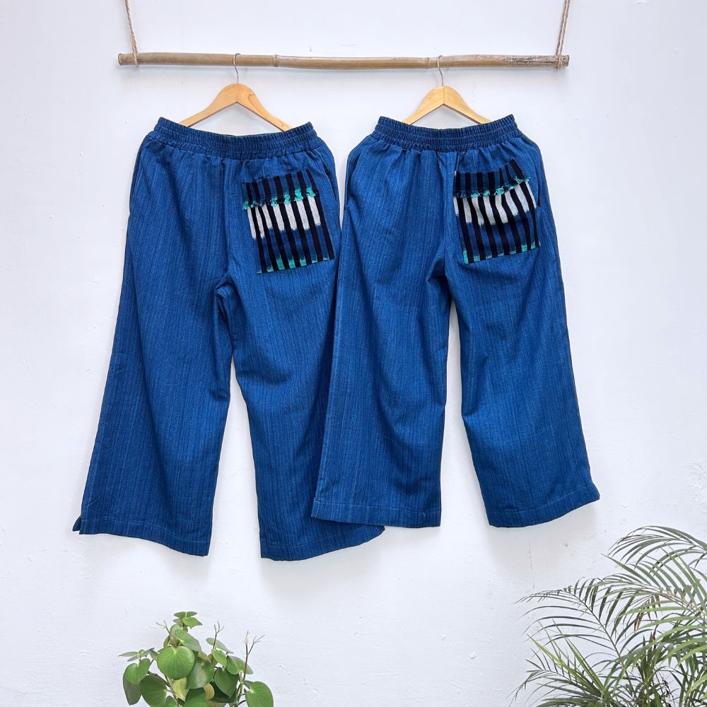 Pair of blue pants with striped pockets on hangers against a white background
