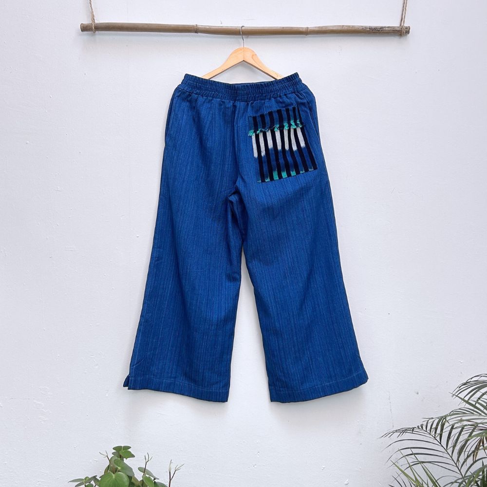 Blue pants with a patch pocket on a hanger against a white wall.