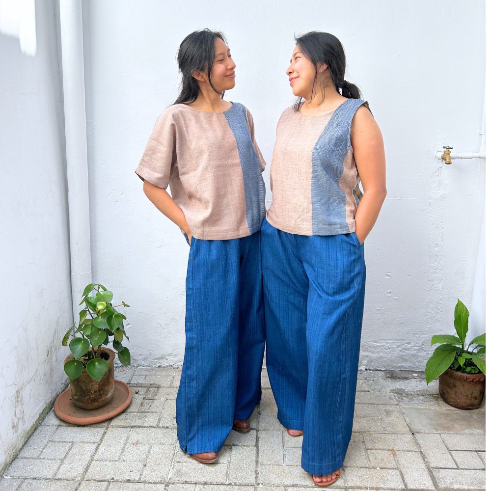 Two women wearing matching outfits with beige tops and blue pants standing against a white wall.