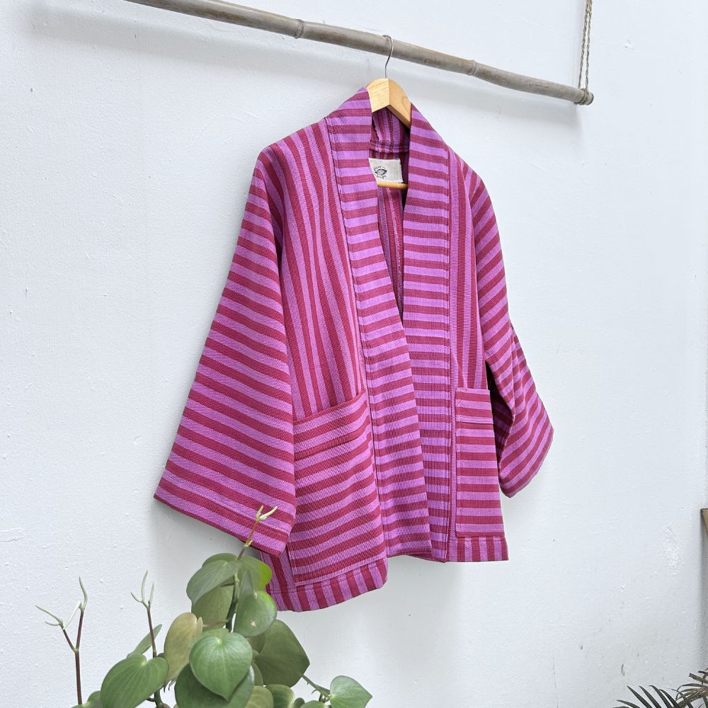 Purple striped garment hanging on a wooden hanger against a white wall with green plants at the bottom.