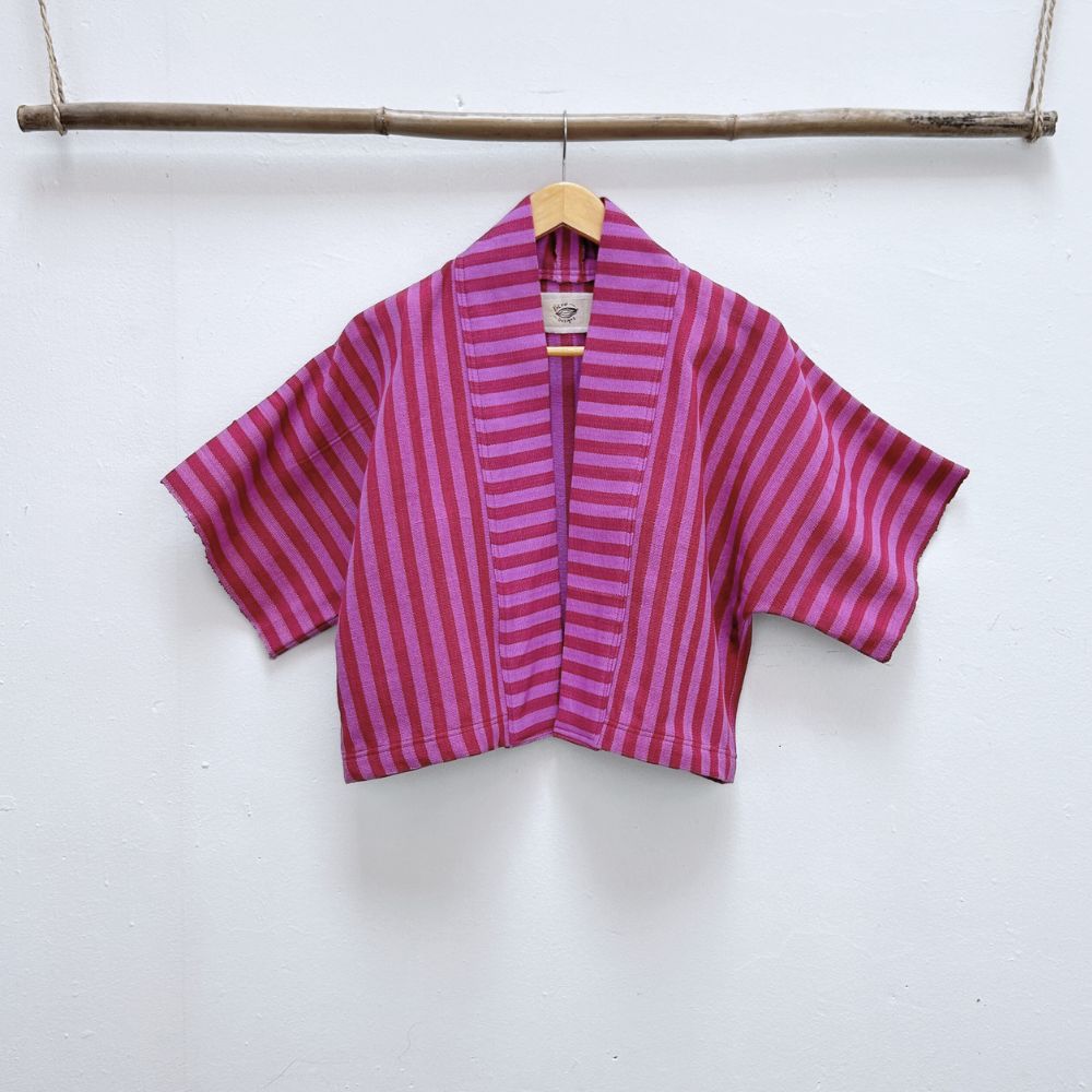 Two Shades of pink striped cropped jacket hanging on a wooden hanger against a white background.