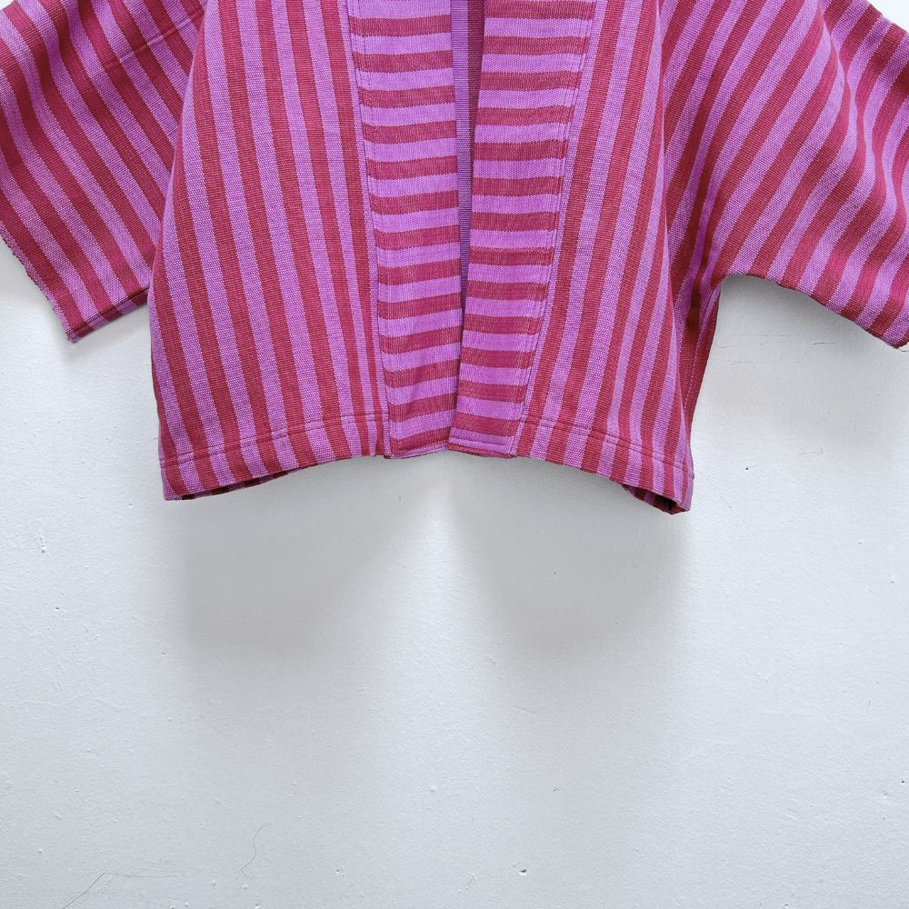 Close-up of Two Shades of pink striped cropped jacket hanging on a wooden hanger against a white background.