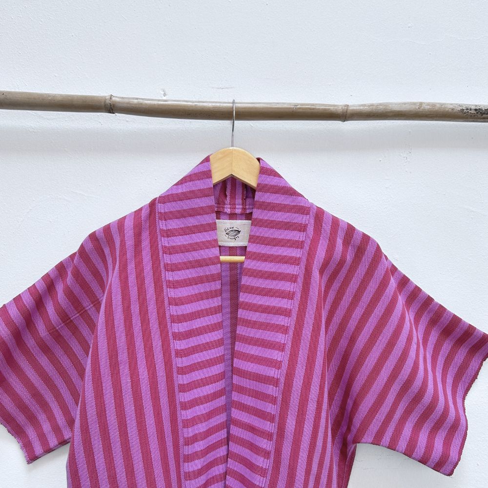 Two Shades of pink striped cropped jacket hanging on a wooden hanger against a white background.