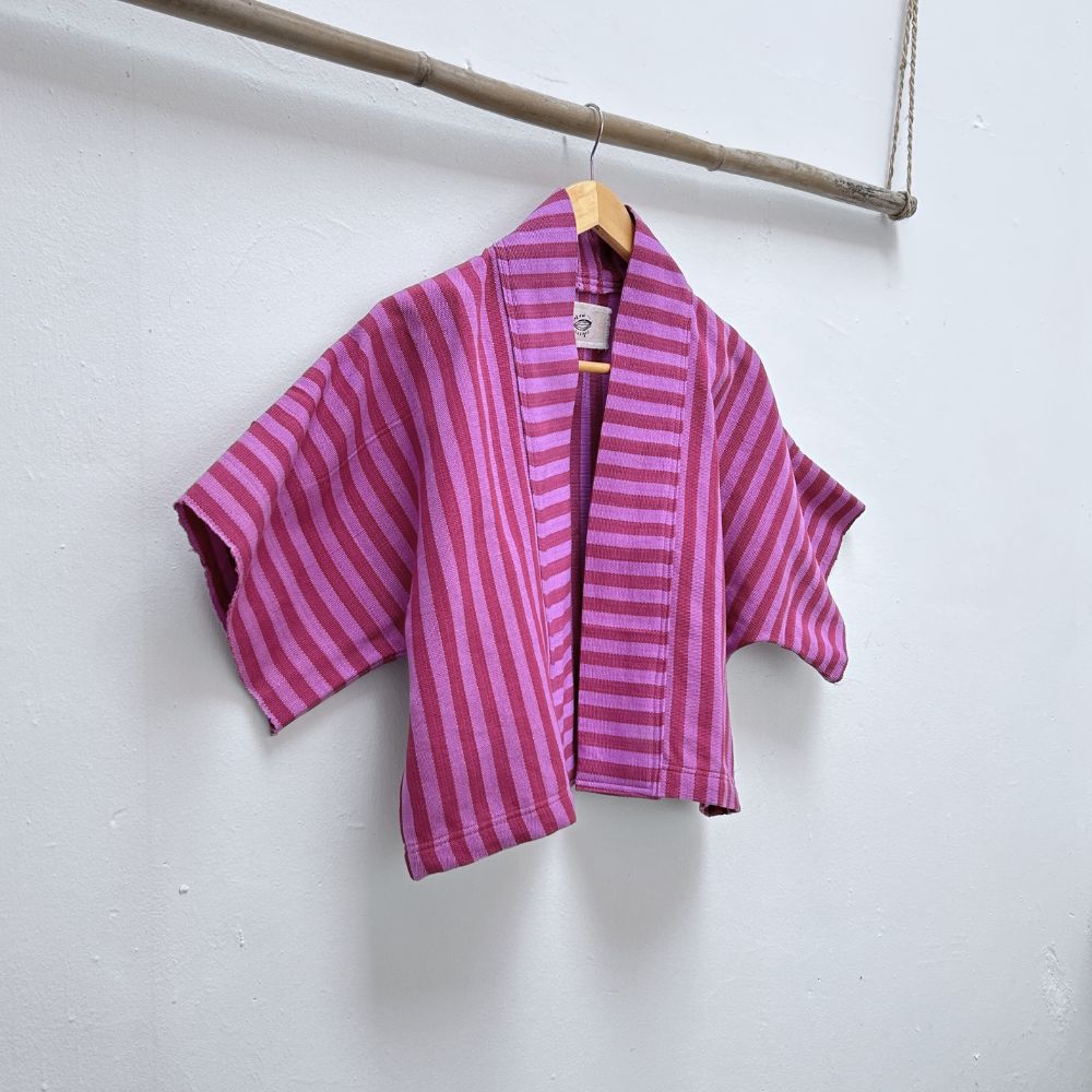 Two Shades of pink striped cropped jacket hanging on a wooden hanger against a white background.