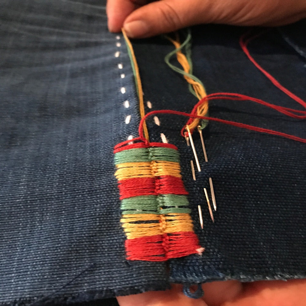 A close-up of embroidery in progress, featuring colorful threads being used on a fabric panel.