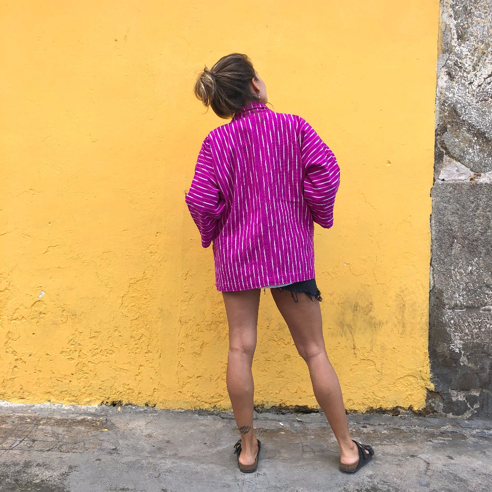 Person wearing a purple and white patterned jacket against a yellow wall.