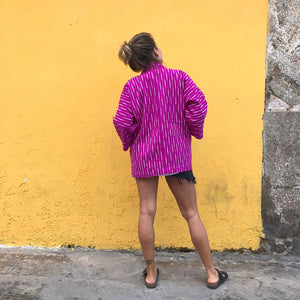 Person wearing a purple and white patterned jacket against a yellow wall.