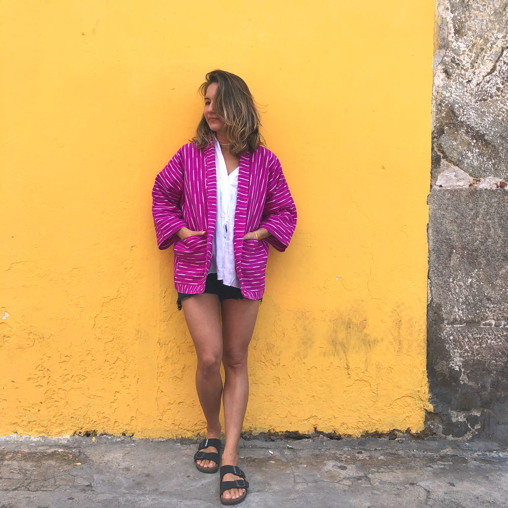 Person wearing a pink jacket standing against a yellow wall.