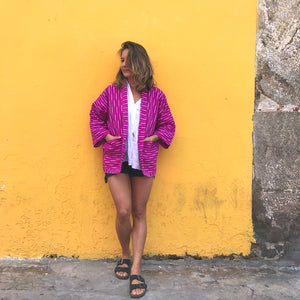 Person wearing a pink jacket standing against a yellow wall.