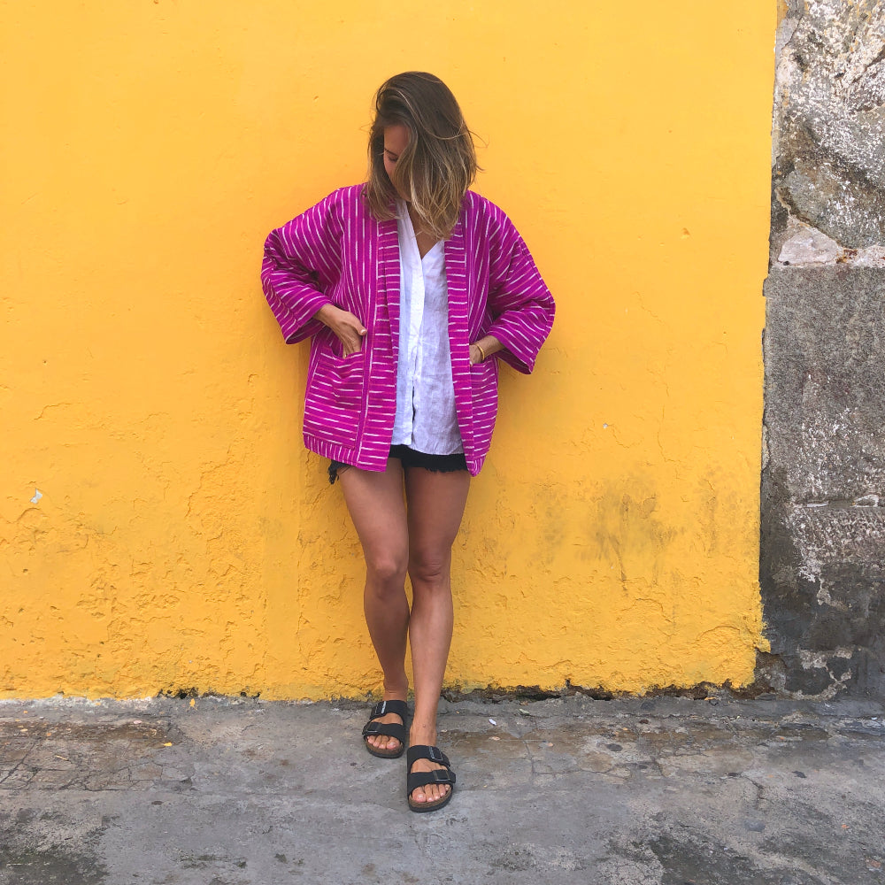 Woman wearing a pink and white patterned jacket against a yellow wall.