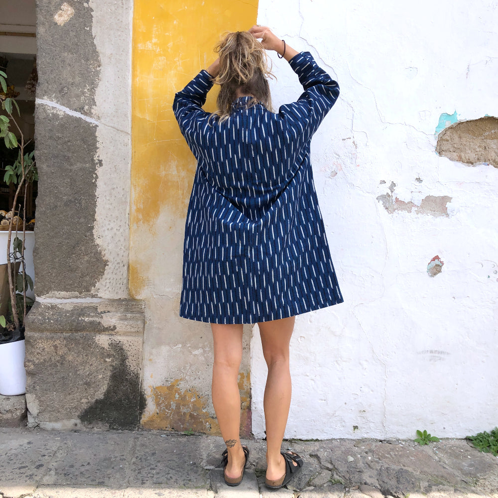 Person wearing a blue patterned jacket standing against a textured wall.