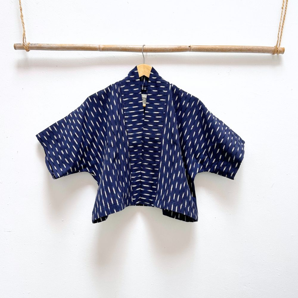 Indigo blue jacket with white  ikat pattern hanging on a wooden rod against a white background