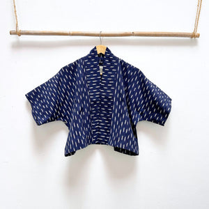 Indigo blue jacket with white  ikat pattern hanging on a wooden rod against a white background