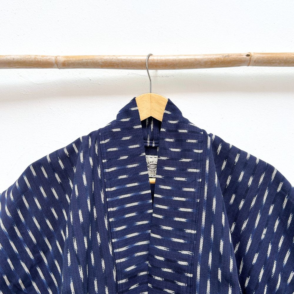 Indigo blue jacket with white ikat pattern hanging on a wooden rod against a white background