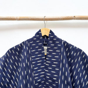 Indigo blue jacket with white ikat pattern hanging on a wooden rod against a white background