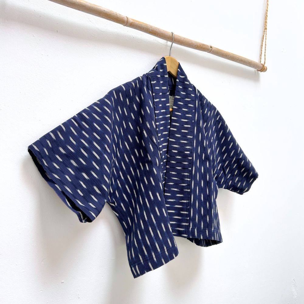 Indigo blue jacket with white  ikat pattern hanging on a wooden rod against a white background