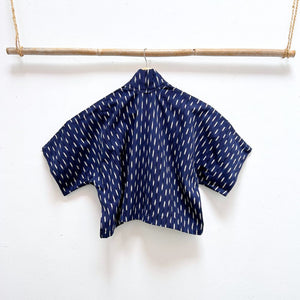 Indigo blue jacket with white  ikat pattern hanging on a wooden rod against a white background