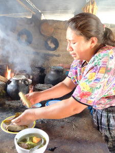 Person cooking over an open flame with pots and pans on a rustic outdoor stove.
