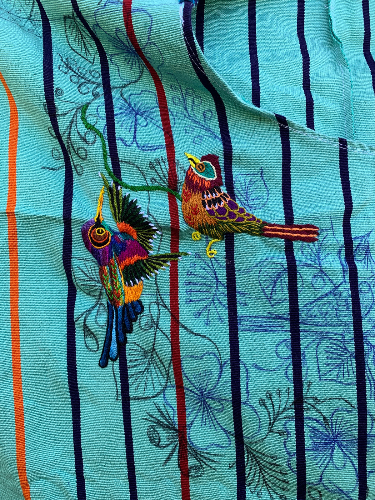 Colorful birds embroidered on a soft green huipil base