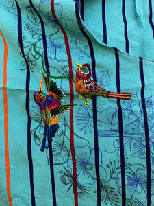Colorful birds embroidered on a soft green huipil base