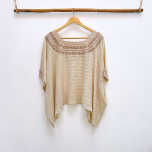 Beige base woven blouse with embroidery french knot neckline  same color on a wooden hanger against a white wall.