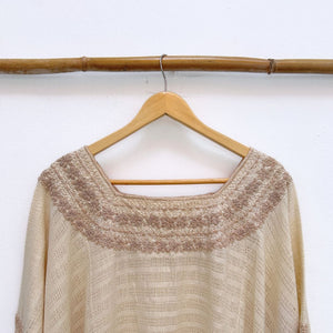 Beige base woven blouse with embroidery french knot neckline  same color on a wooden hanger against a white wall.