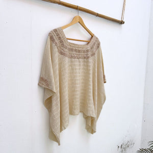 Beige base woven blouse with embroidery french knot neckline  same color on a wooden hanger against a white wall.