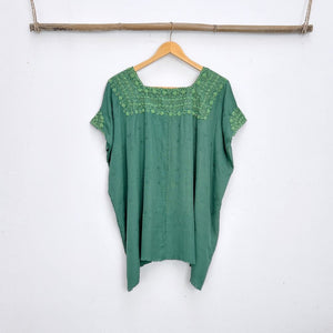 Green top with embroidered neckline on a wooden hanger against a white background