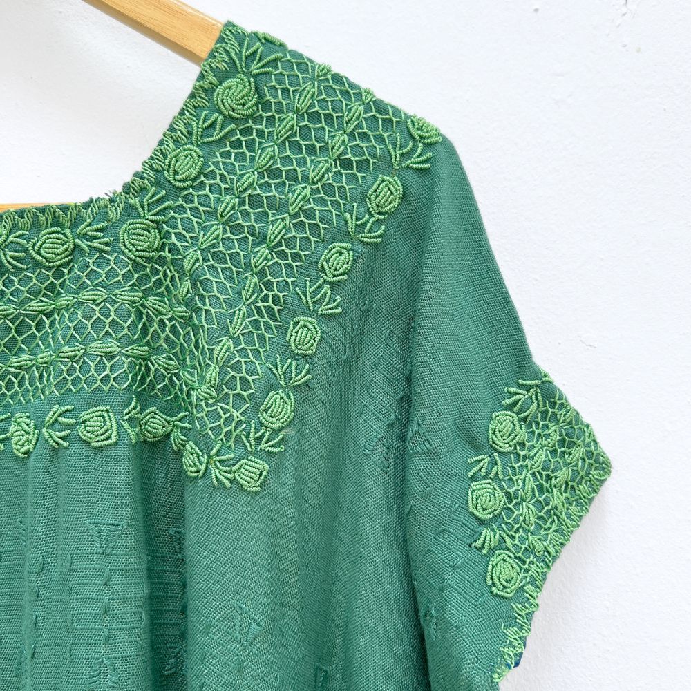 Green top with embroidered neckline on a wooden hanger against a white background