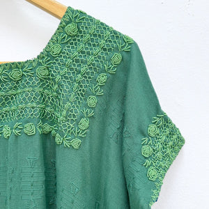 Green top with embroidered neckline on a wooden hanger against a white background