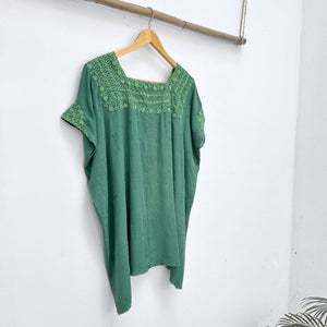 Green top with embroidered neckline on a wooden hanger against a white background