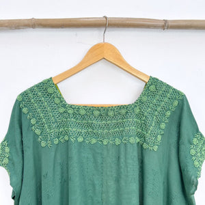 Green top with embroidered neckline on a wooden hanger against a white background