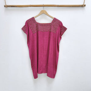 Magenta base woven blouse with embroidery french knot neckline   on a wooden hanger against a white wall.
