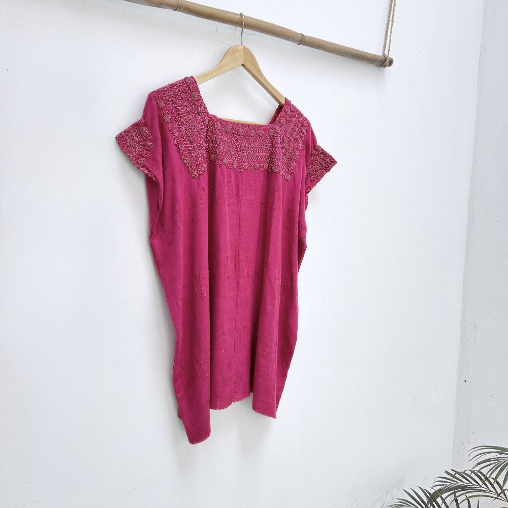 Magenta base woven blouse with embroidery french knot neckline  same color on a wooden hanger against a white wall.

