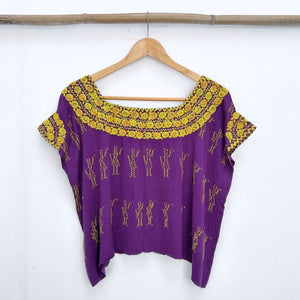 Purple blouse with yellow floral french knot embroidery on a wooden hanger against a white background