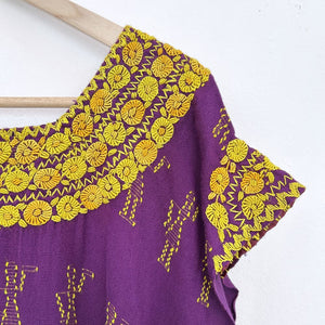 Purple blouse with yellow floral french knot embroidery on a wooden hanger against a white background