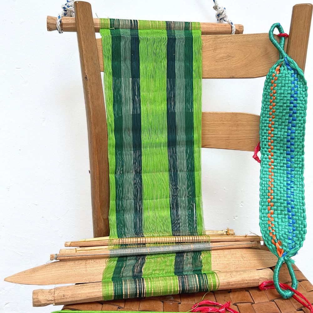 Wooden chair with a loom in green hues and colorful yarn on a white background 
