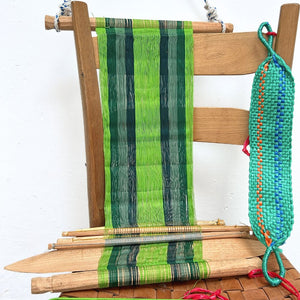Wooden chair with a loom in green hues and colorful yarn on a white background 