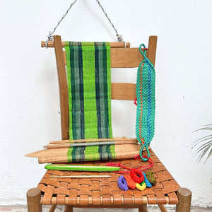 Wooden chair with a loom in green hues and colorful yarn on a white background